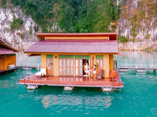 two people standing on a house on a dock in the water at Panvaree Resort in Ratchaprapha
