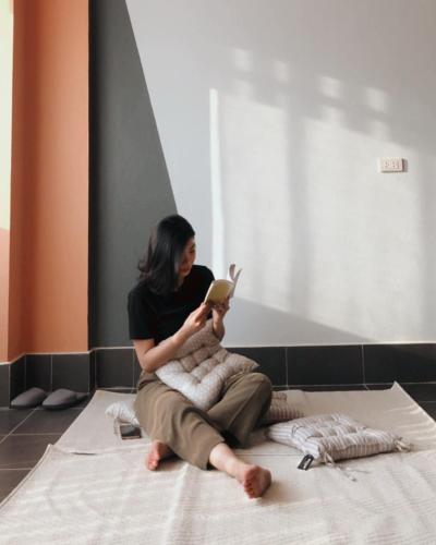 a woman sitting on a bed reading a book at HideSeek Hostel Vientiane Thai embassy in Vientiane