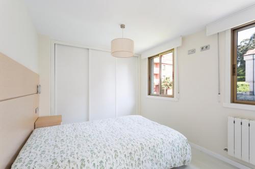 a white bedroom with a bed and two windows at Housingcoruña Apartamento Playa Miño 04 in Miño