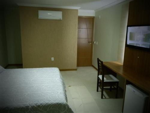 a bedroom with a bed and a desk and a television at Setiba Pousada Park in Guarapari