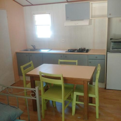 a kitchen with a wooden table and green chairs at mobilhome lac de vassiviere in Faux-la-Montagne