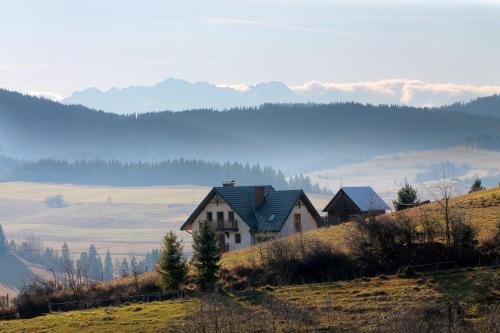 a house on the side of a hill with mountains in the background at Domek na wzgórzu in Łapsze Niżne