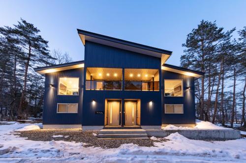a blue house in the woods in the snow at Firefly Apartments in Hakuba