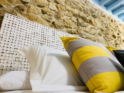 a bed with yellow and white pillows next to a stone wall at LA CASA REBONITA in Candelario