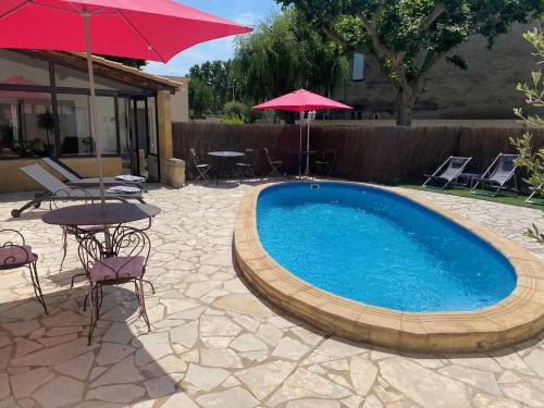 a swimming pool with tables and chairs and an umbrella at L'Escale des Alpilles in Rognonas