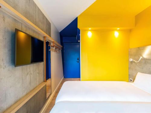 a room with a bed with a yellow wall and a tv at ibis budget Fontainebleau Avon in Avon