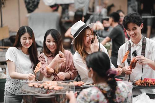 eine Gruppe von Menschen steht um einen Tisch herum und isst in der Unterkunft Noursabah Boutique Bed Bangkok in Bangkok