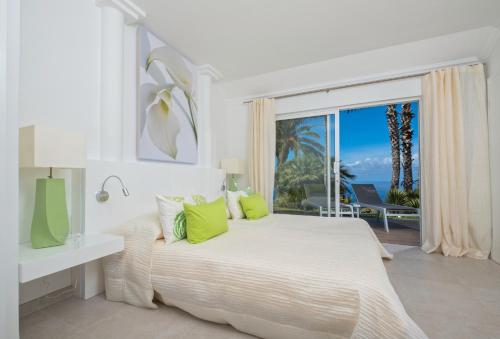 Dormitorio blanco con cama y ventana grande en Jardin de la Paz en La Matanza de Acentejo