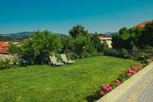 two white chairs sitting on a lawn with flowers at Casa Victória in Ponte da Barca