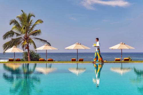a woman walking by a swimming pool next to the ocean at Jetwing Lighthouse, A Luxury Reserve in Galle