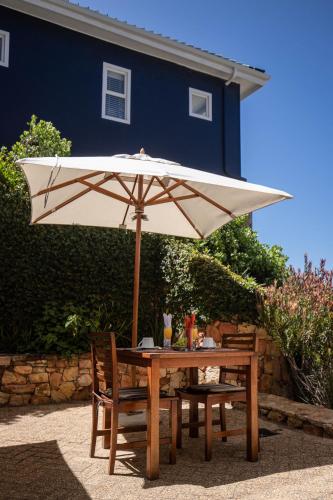 a wooden table with an umbrella and two chairs at Simon’s Town Guest House in Simonʼs Town