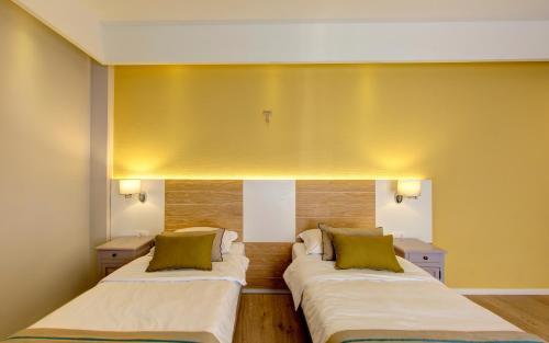 two beds in a room with yellow walls at Hotel Villa Regina in Međugorje