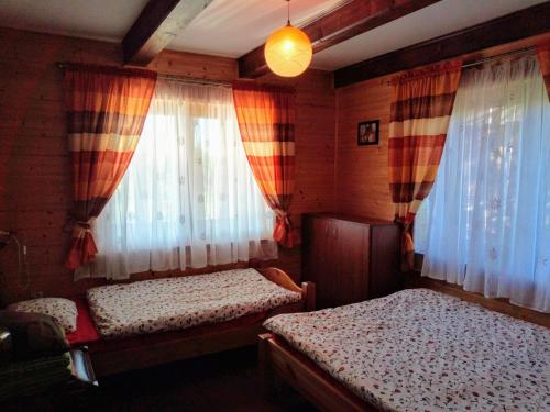 a bedroom with two beds and two windows at Świerkowe Chatki - Apartament Kominkowy in Olchowiec