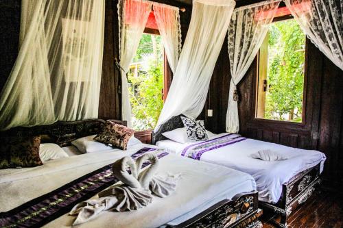 two beds in a room with windows and curtains at The Antique Riverside Resort in Ban Pong