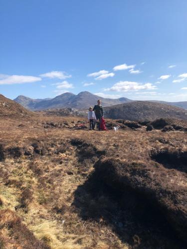 
two people are sitting on a hill with a mountain at Letterfrack Farm Lodge house in Letterfrack village Connemara in Letterfrack
