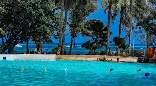 a swimming pool with a beach and palm trees at Papillon Lagoon Reef Hotel in Diani Beach