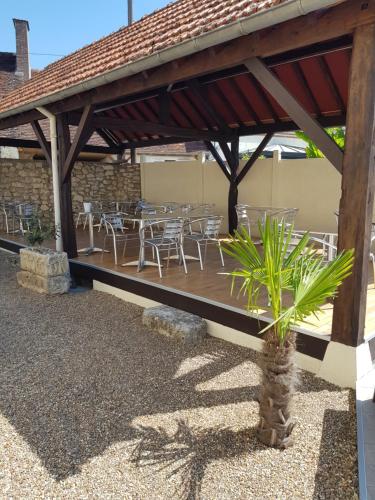 a wooden deck with tables and chairs and a palm tree at Hôtel Restaurant Le Moulin de la Renne Adults Only proche Zoo de Beauval in Thésée