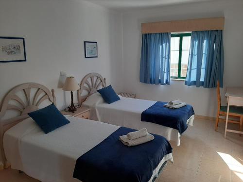 um quarto com 2 camas com cortinas azuis e uma mesa em Duna do Alvor Apartment 322 em Alvor