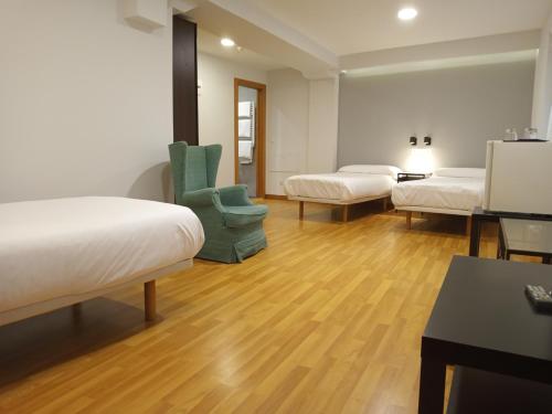 Habitación con 3 camas y una silla verde. en Pensión Begoña - centro ciudad, en Bilbao