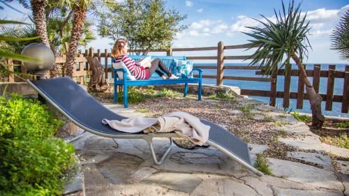 a woman sitting on a blue bench next to the ocean at Casa Delta delle Acque Vista spettacolare e Giardino in Cala Gonone