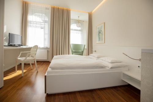 a white bedroom with a bed and a desk at Hotel Gollner in Graz