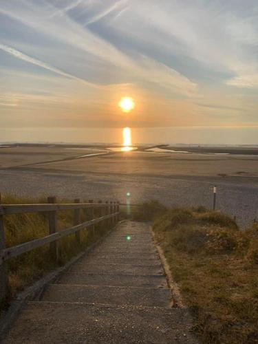 a sunset over a field with a path and a fence at ‘t Ziltebos in Wenduine