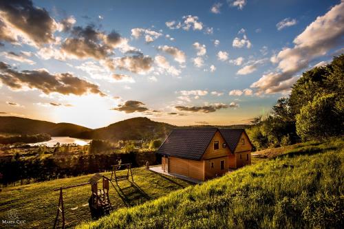 a house on a hill with the sun setting behind it at Chaty na Cholewicy Domki Całoroczne in Solina