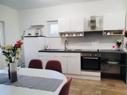 a kitchen with white cabinets and a table with red chairs at Apartman Školj in Jovići
