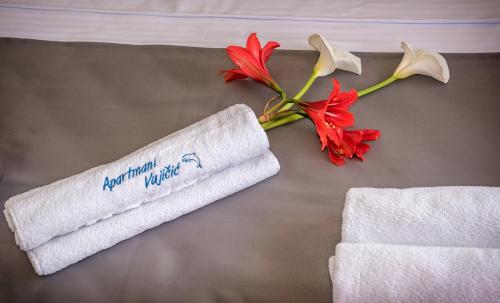 a roll of towels and a flower on a bed at Apartments Vujicic in Tivat