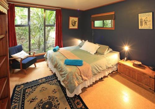 a bedroom with a bed and a chair and windows at Waiheke Escape in Palm Beach