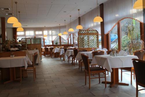 a restaurant with white tables and chairs and windows at Kurpark Flair Hotel Im Ilsetal in Ilsenburg