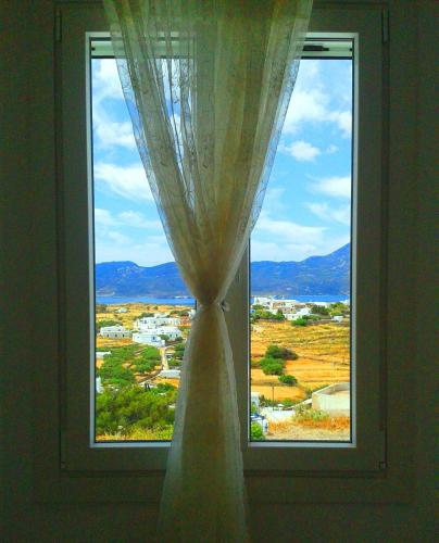 a window with a curtain and a view of a town at Georgia Rooms Milos in Plaka Milou