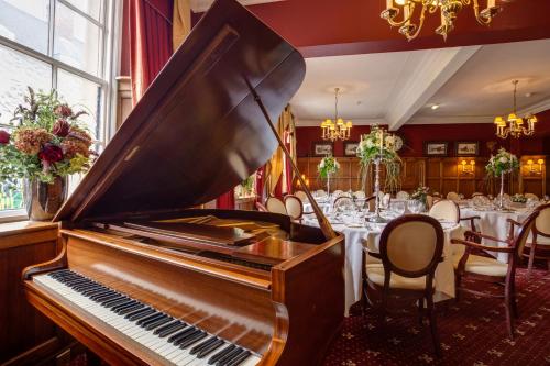 a piano in a room with tables and chairs at The Saracens Head Hotel in Southwell