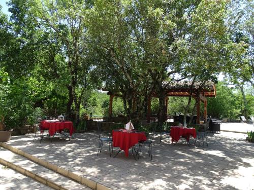 a patio with red tables and chairs under a tree at Hôtel Mas de l'Espaïre in Les Vans