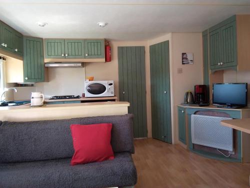 - une cuisine avec des placards verts et un canapé avec un oreiller rouge dans l'établissement Chalet plage Lomer, à Pénestin