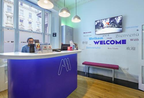 a man sitting at a counter at a welcome center at Astor Victoria Hostel in London