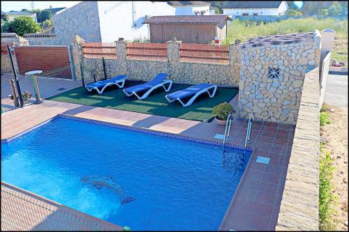 a swimming pool with two blue chairs next to a stone wall at Chalet Puente de Tabla in Conil de la Frontera