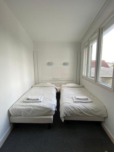 two beds in a small room with two windows at Hotel du Centre Lucé Chartres in Luce