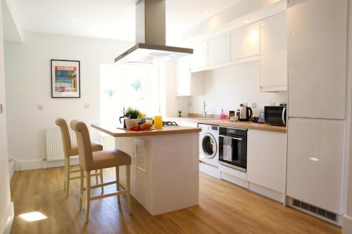 a kitchen with white cabinets and a counter with chairs at Modern New House - Great Location - Garden - Parking - Fast WiFi - Smart TV - Stunning 2 Bedroom House sleeps up to 4! Only 5 mins drive to Sandbanks Beach in Parkstone