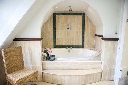 a bathroom with a bath tub and a chair at Langshott Manor - Luxury Hotel Gatwick in Horley