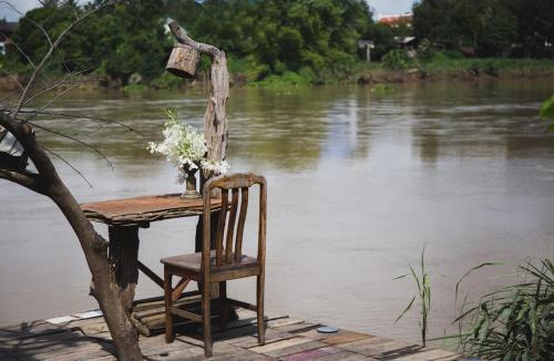 uma mesa com uma cadeira sentada ao lado de um rio em The Antique Riverside Resort em Ban Pong