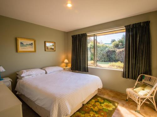 a bedroom with a bed and a window and a chair at Tasman Treat - Marahau Holiday Home in Marahau