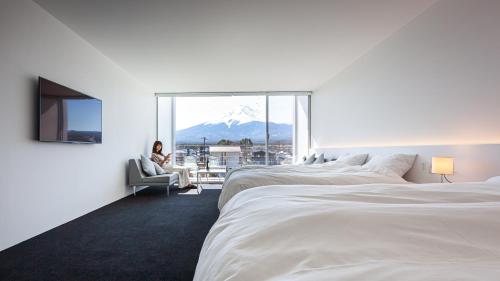 a woman sitting in a chair in a hotel room with two beds at THE GARDEN in Fujikawaguchiko