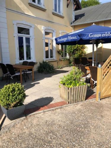 a patio with a table and a blue umbrella at Landgasthaus Streichmühle in Dollerup