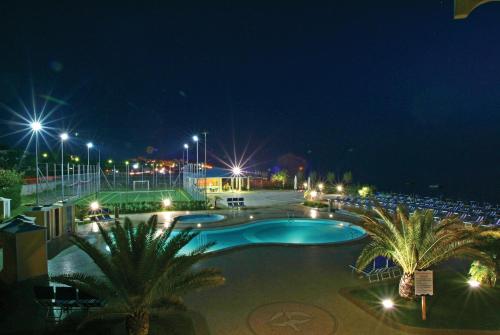 a swimming pool at night with palm trees and chairs at Hotel dei Focesi in Diamante