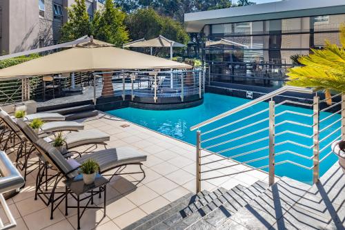 an outdoor swimming pool with chairs and an umbrella at City Lodge Hotel Johannesburg Airport, Barbara Road in Kempton Park