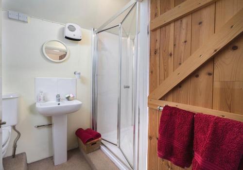 a bathroom with a sink and a shower with red towels at The Nook at West Langton lodge in Market Harborough