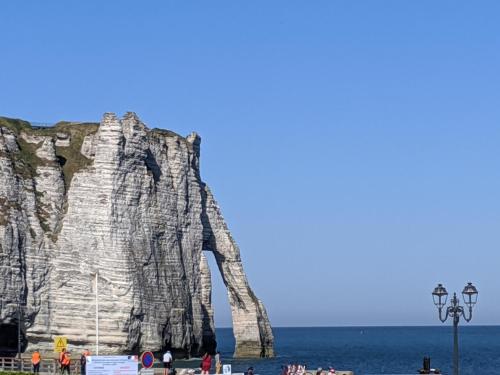 a large rock formation in the ocean with people on the beach at L'Aiguille Creuse in Étretat