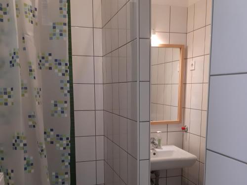 a white tiled bathroom with a sink and a mirror at LÁSZLÓ Turistaszálló in Visegrád