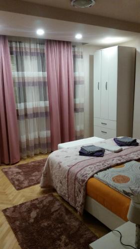 a bedroom with a bed and a cabinet and curtains at Apartman Lux K in Bijeljina